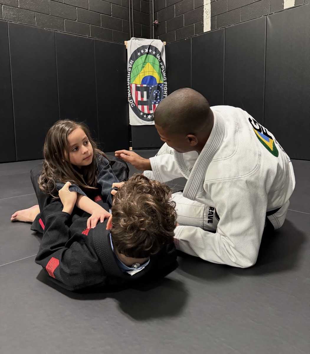 Coach guiding two young students through a technique during a kids jiu-jitsu class at WDC BJJ
